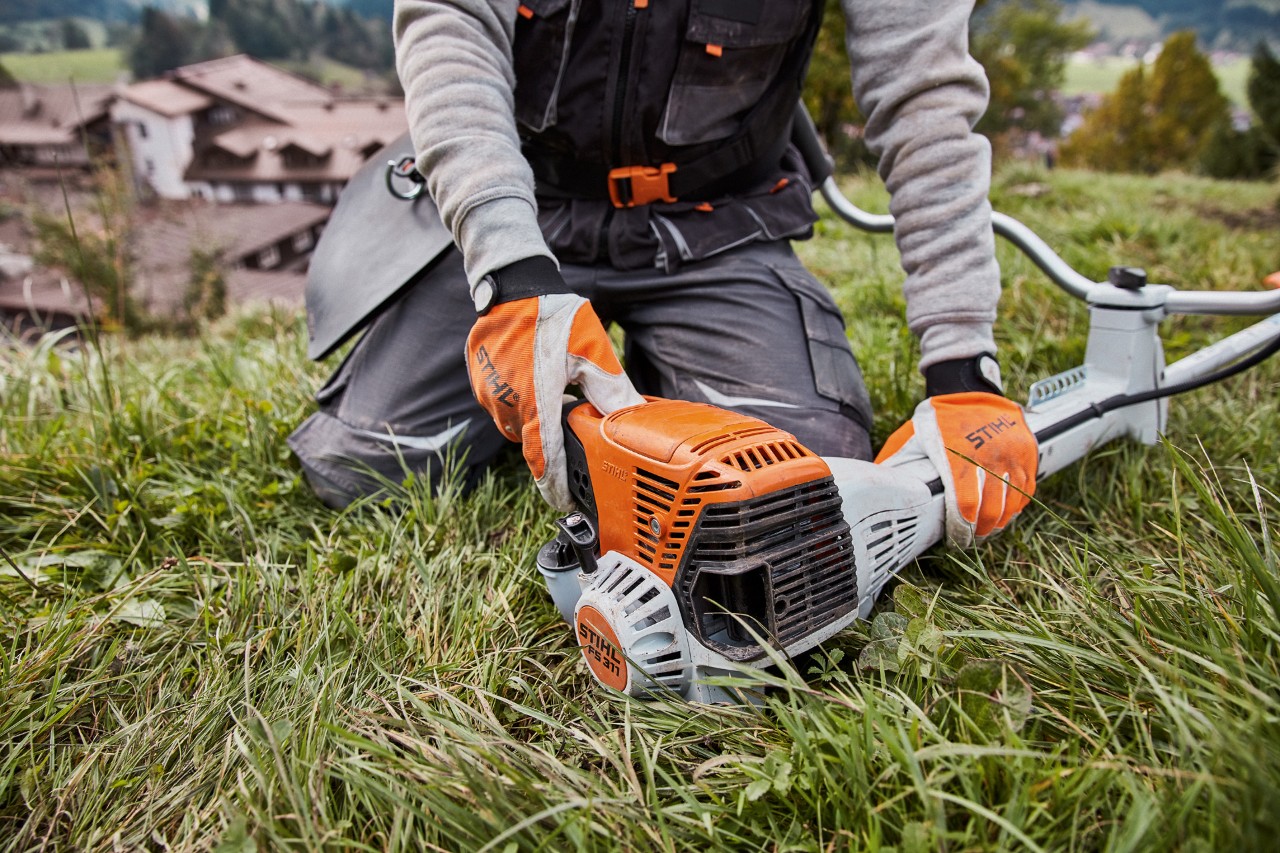Una persona con guantes arrodillada en el suelo comprueba una desbrozadora STIHL FS 311