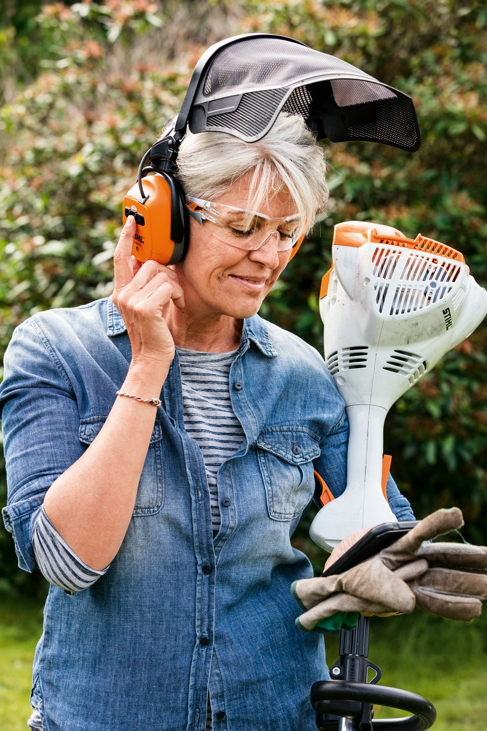 Una mujer con pantalla y cascos protectores STIHL DYNAMIC BT-N sostiene una desbrozadora de gasolina STIHL FS 58 R