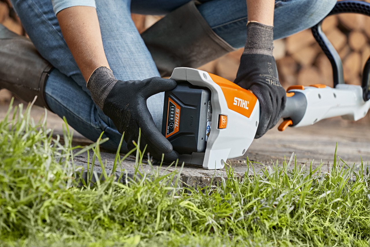 Una persona de rodillas retira la batería de una motoguadaña de batería STIHL FSA 57