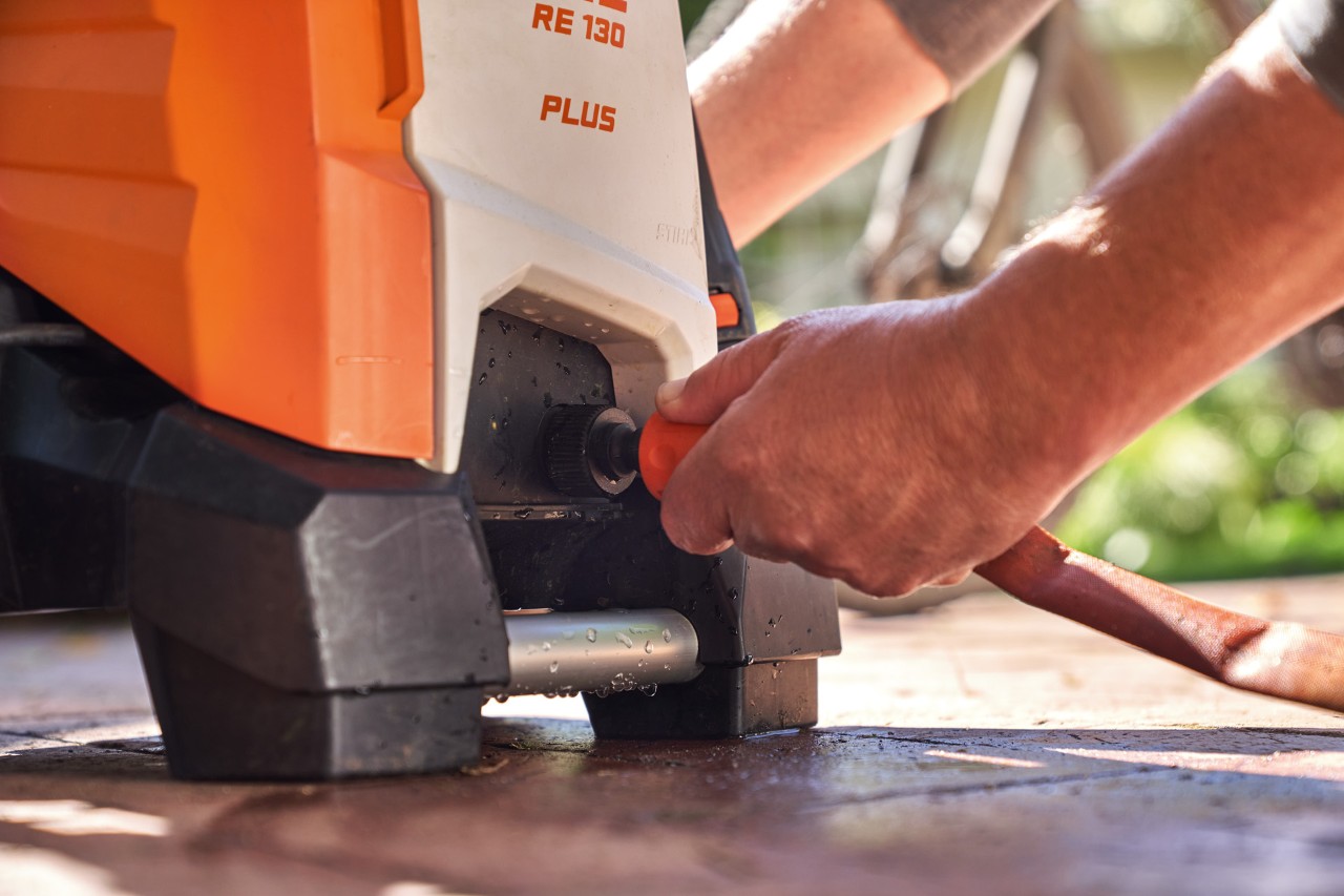 Una persona está conectando una manguera de riego a la hidrolimpiadora STIHL RE 130 PLUS