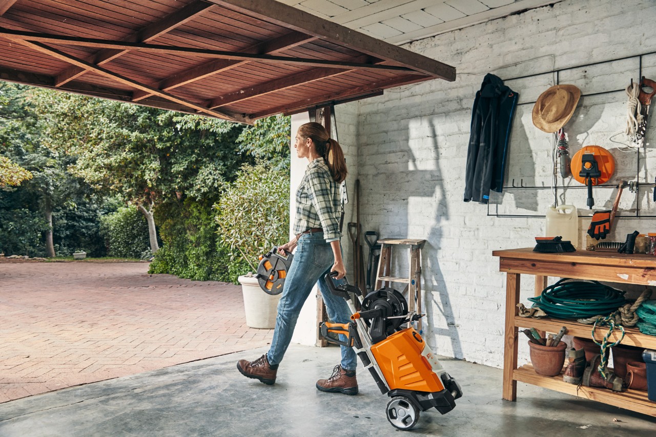 Una mujer sale de un garaje con la hidrolimpiadora STIHL RE 130 PLUS
