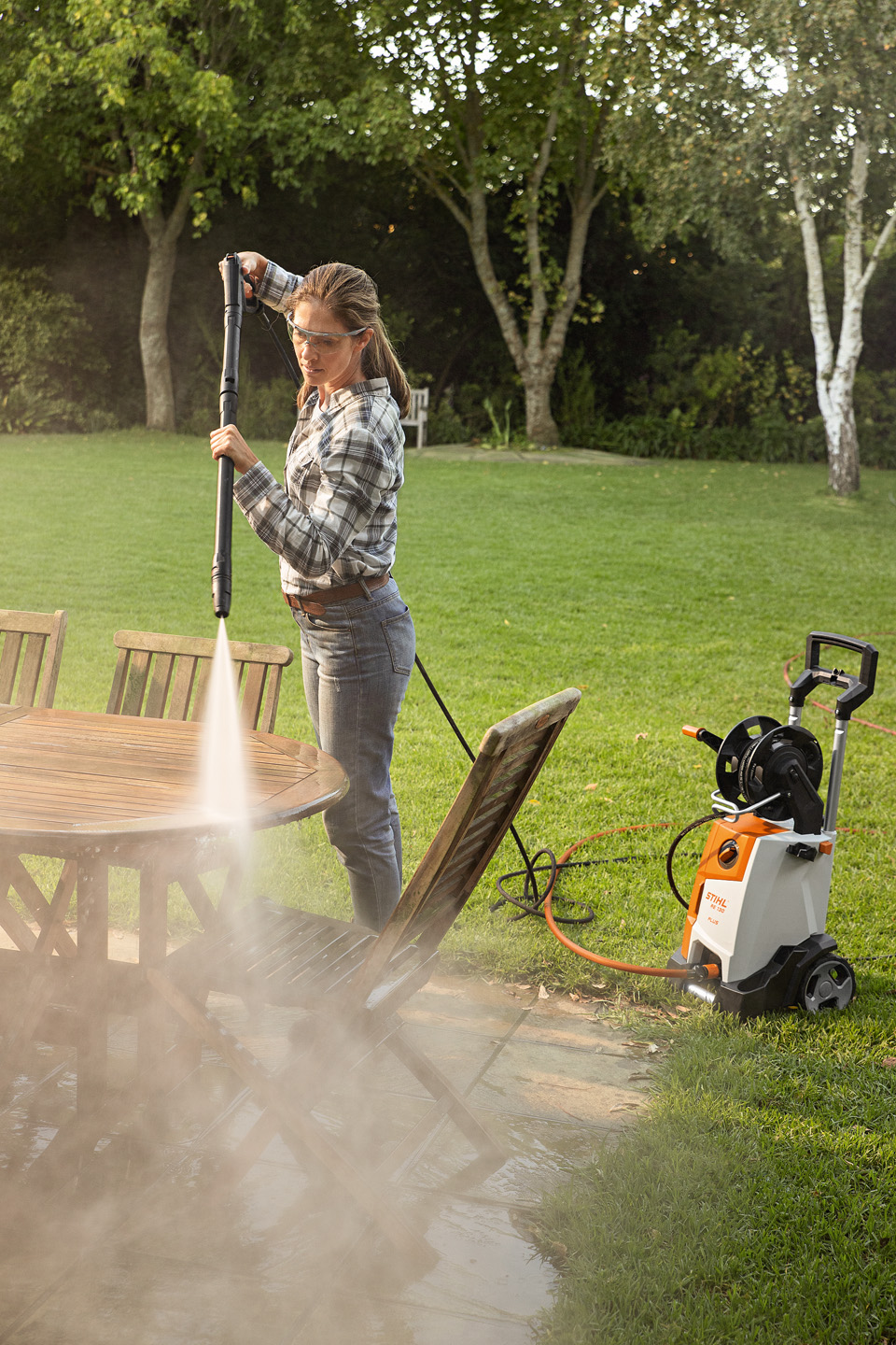 Una mujer limpia muebles de jardín en el exterior con la hidrolimpiadora STIHL RE 130 PLUS