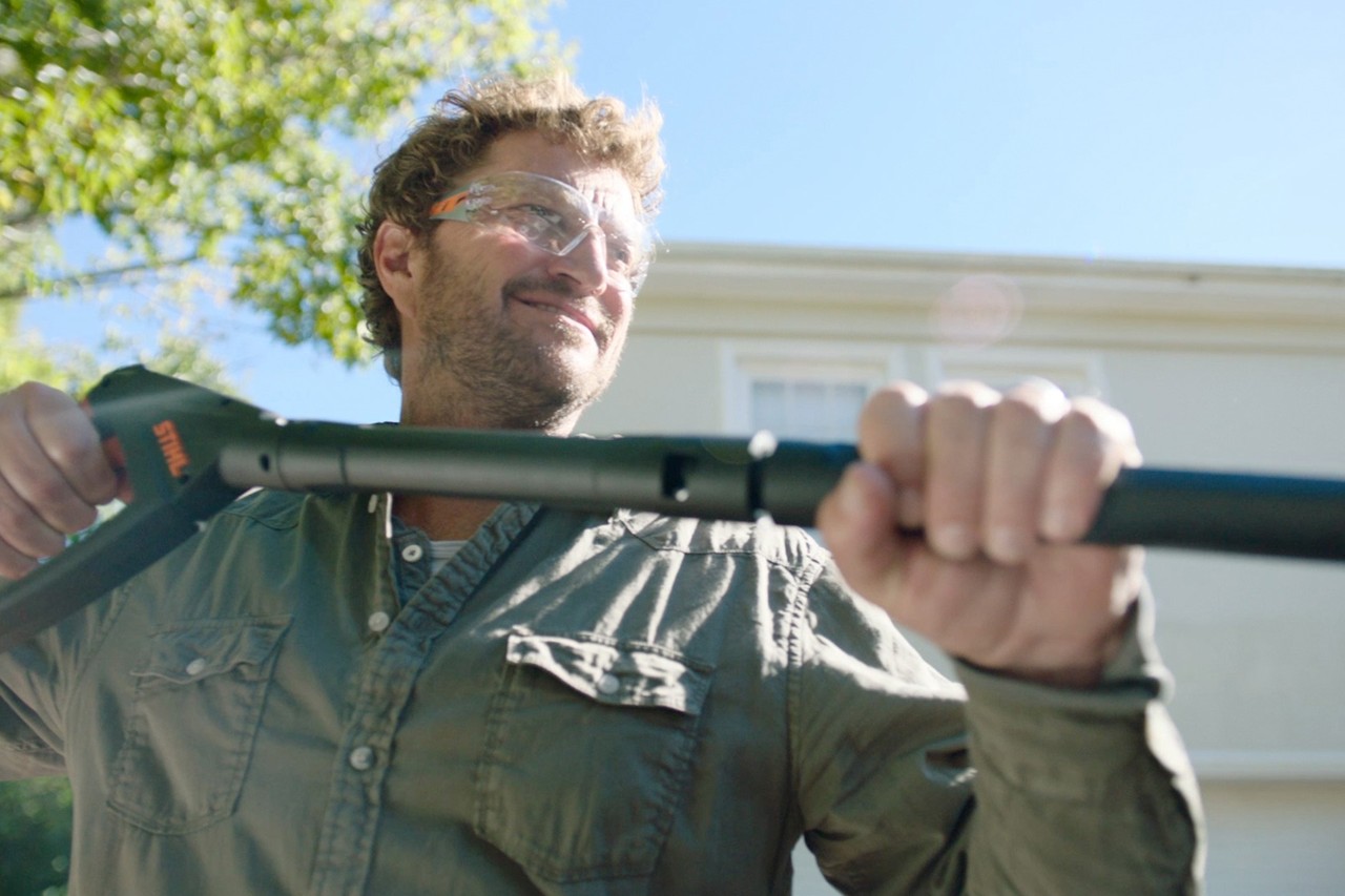 Un hombre con gafas protectoras sujeta la hidrolimpiadora STIHL RE 130 PLUS; en segundo plano, una casa  