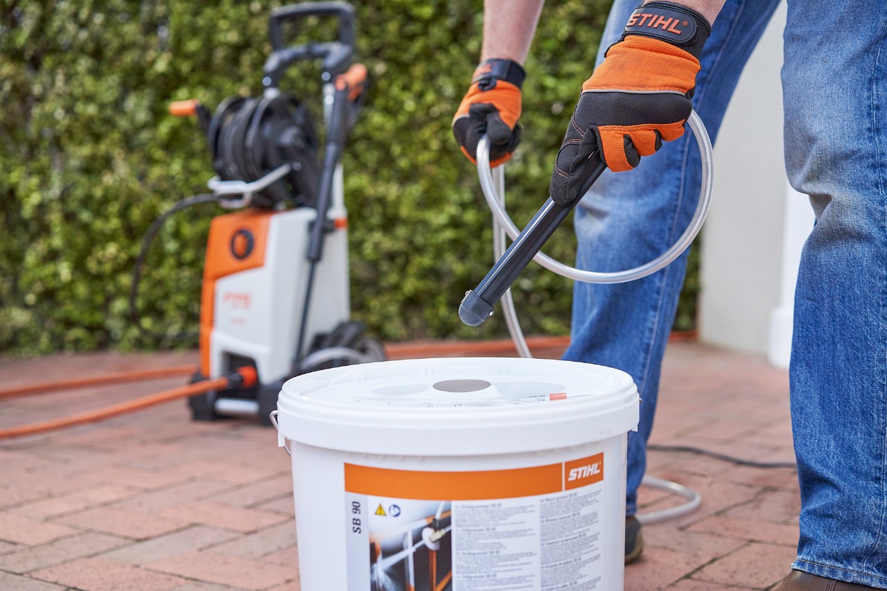 Un hombre con guantes de protección frente a un seto de jardín utiliza el granulado de pulverización STIHL SB 90 