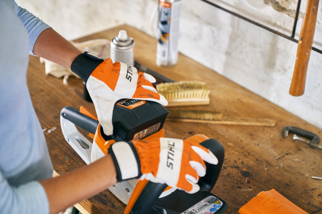 Persona trabajando con guantes en el cortasetos de batería STIHL HSA 56 junto a una lima para afilar cortasetos