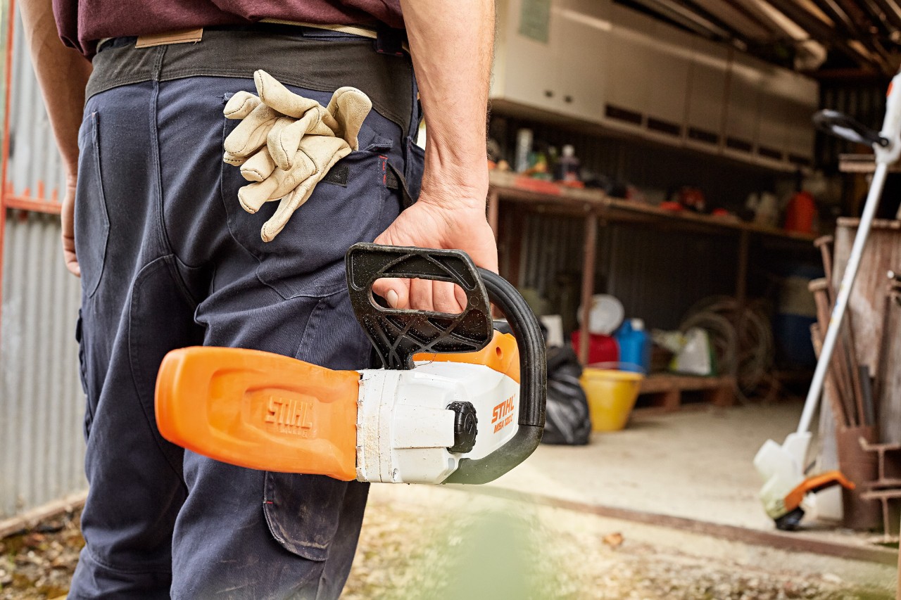 Un hombre entrando en un taller con una motosierra de batería STIHL con protector de espada en la mano