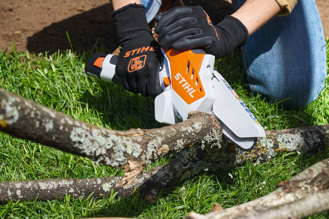 Una persona con guantes de protección corta ramas en trozos con una minisierra de batería STIHL GTA 26
