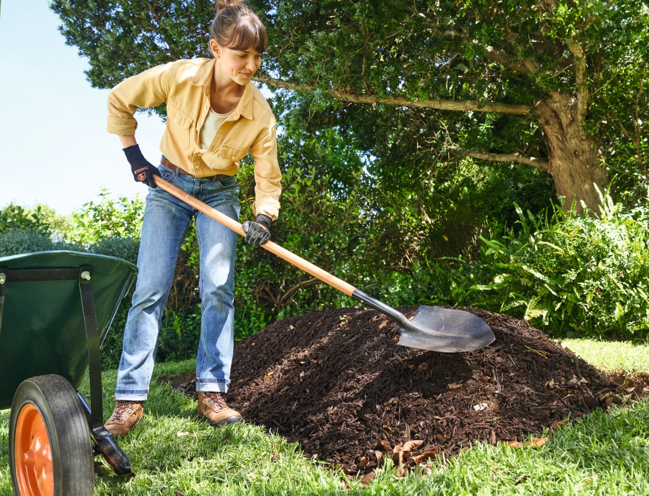 Una mujer coloca una capa de compost grueso en el bancal de cama elevada con la laya