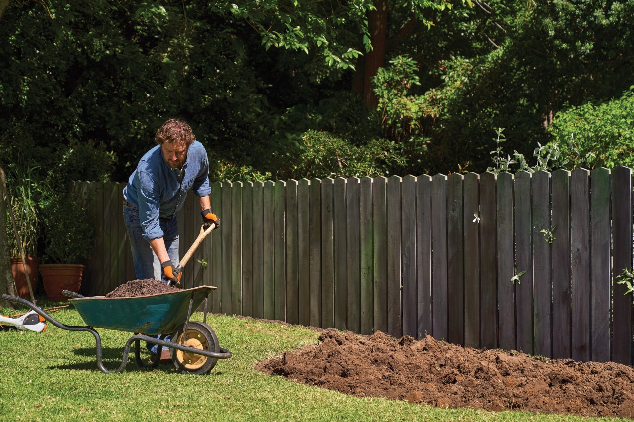 Un hombre añade compost con una pala de una carretilla a un parterre sin plantas