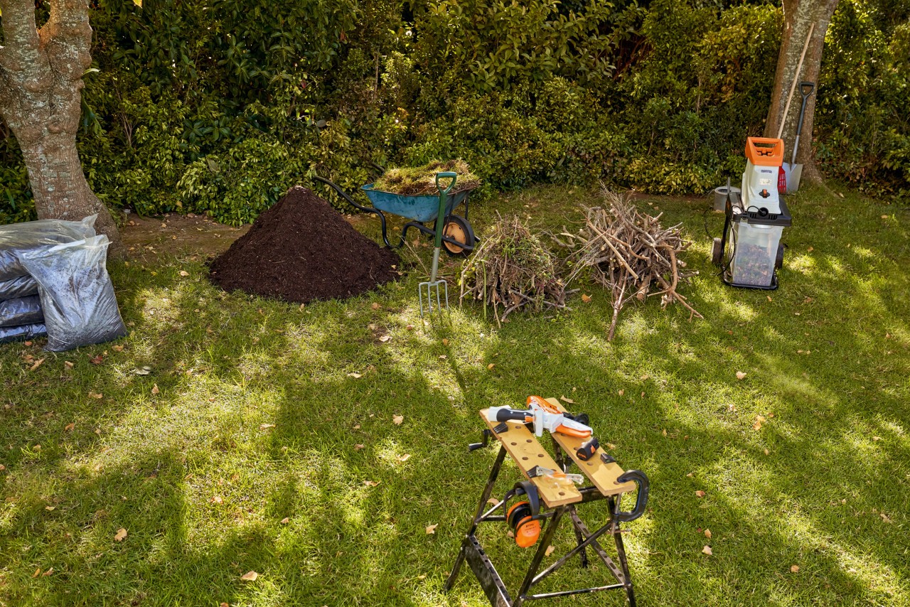 Materiales para rellenar una mesa de cultivo: una biotrituradora eléctrica STIHL GHE 140 y compost en un jardín.