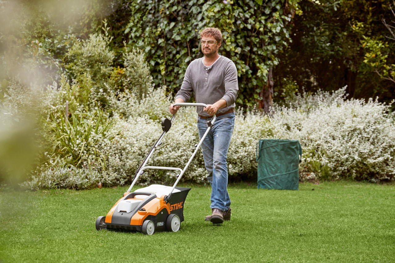 Un hombre escarifica el césped antes de abonarlo con un escarificador STIHL RLE 240