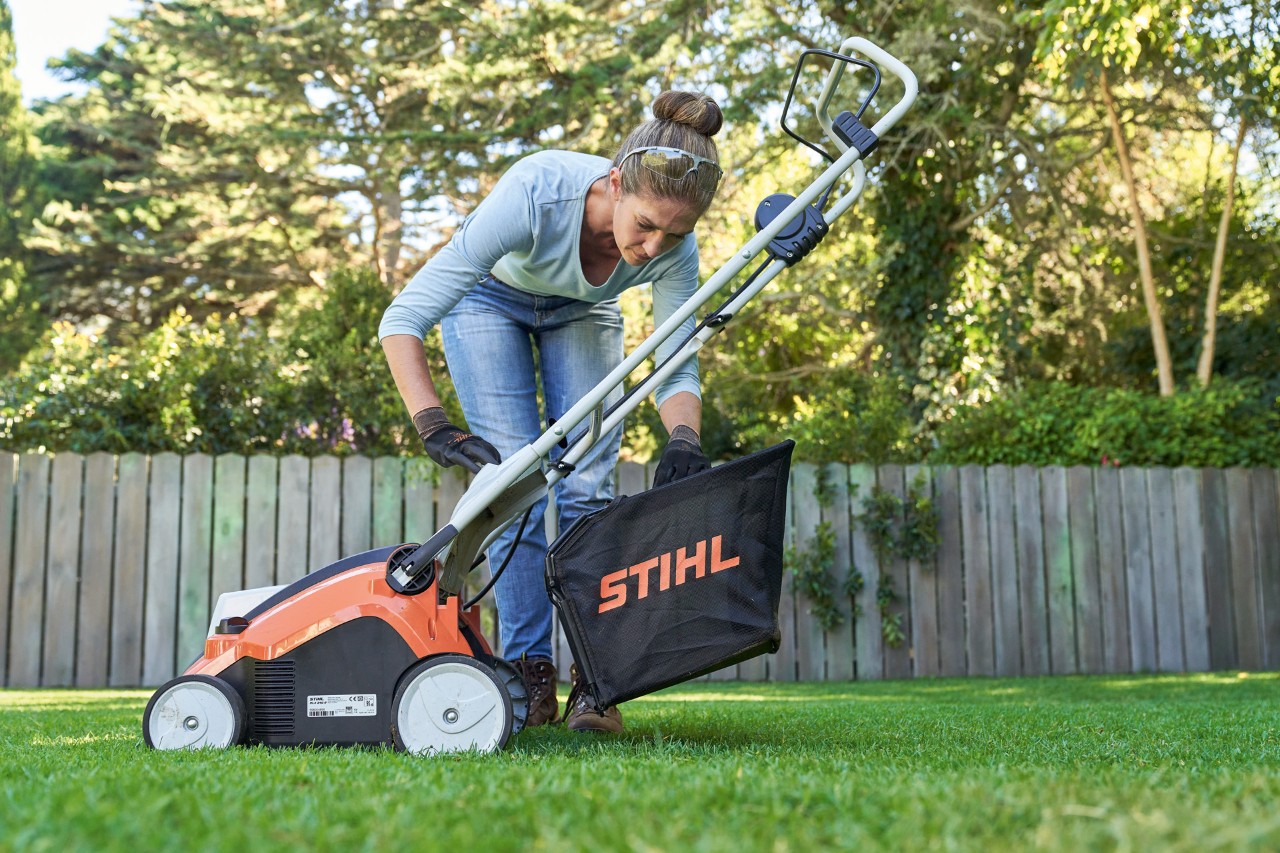 Una mujer cuelga el recogedor del escarificador de batería STIHL RLA 240 en la parte trasera de la máquina.