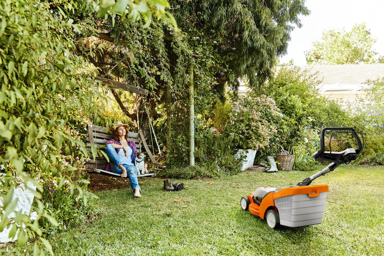 Una mujer se relaja en un columpio junto a un cortacésped de batería STIHL RMA 339 