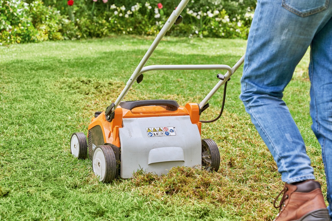 Una mujer escarifica el terreno con un escarificador de césped eléctrico STIHL RLA 240 para replantar césped.