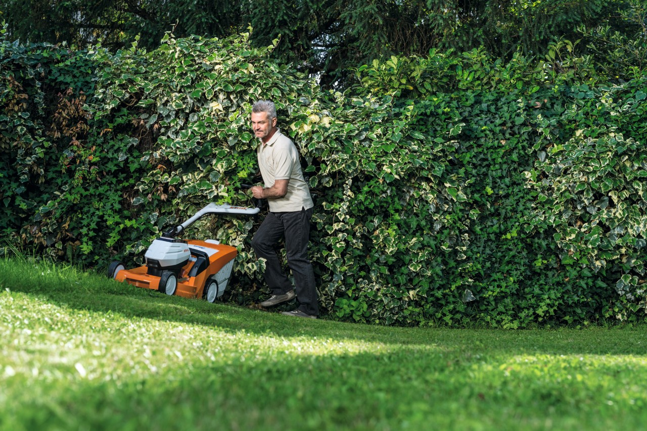 Un hombre corta el césped cuesta arriba con un cortacésped de batería STIHL RMA 448 TC  