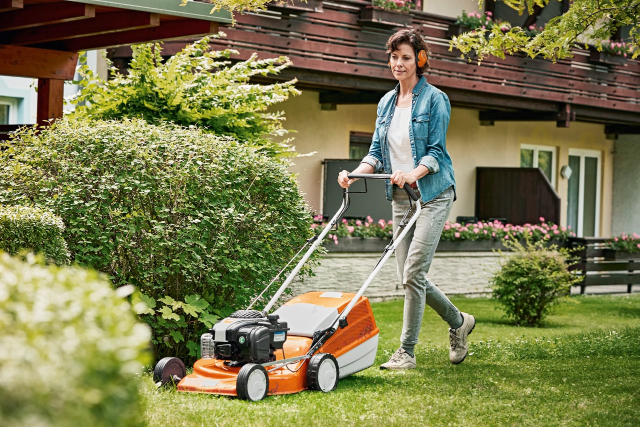 Una mujer se encarga del mantenimiento del césped en primavera con cortacésped de gasolina STIHL RM 243 T 