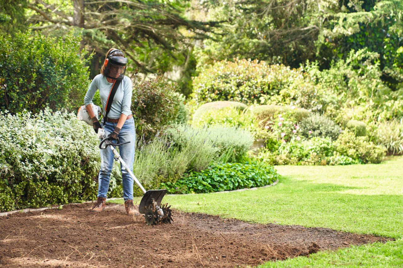 Mujer preparando el suelo para poner rollos de césped con un sistema combinado STIHL KM 56 RC-E con fresadora