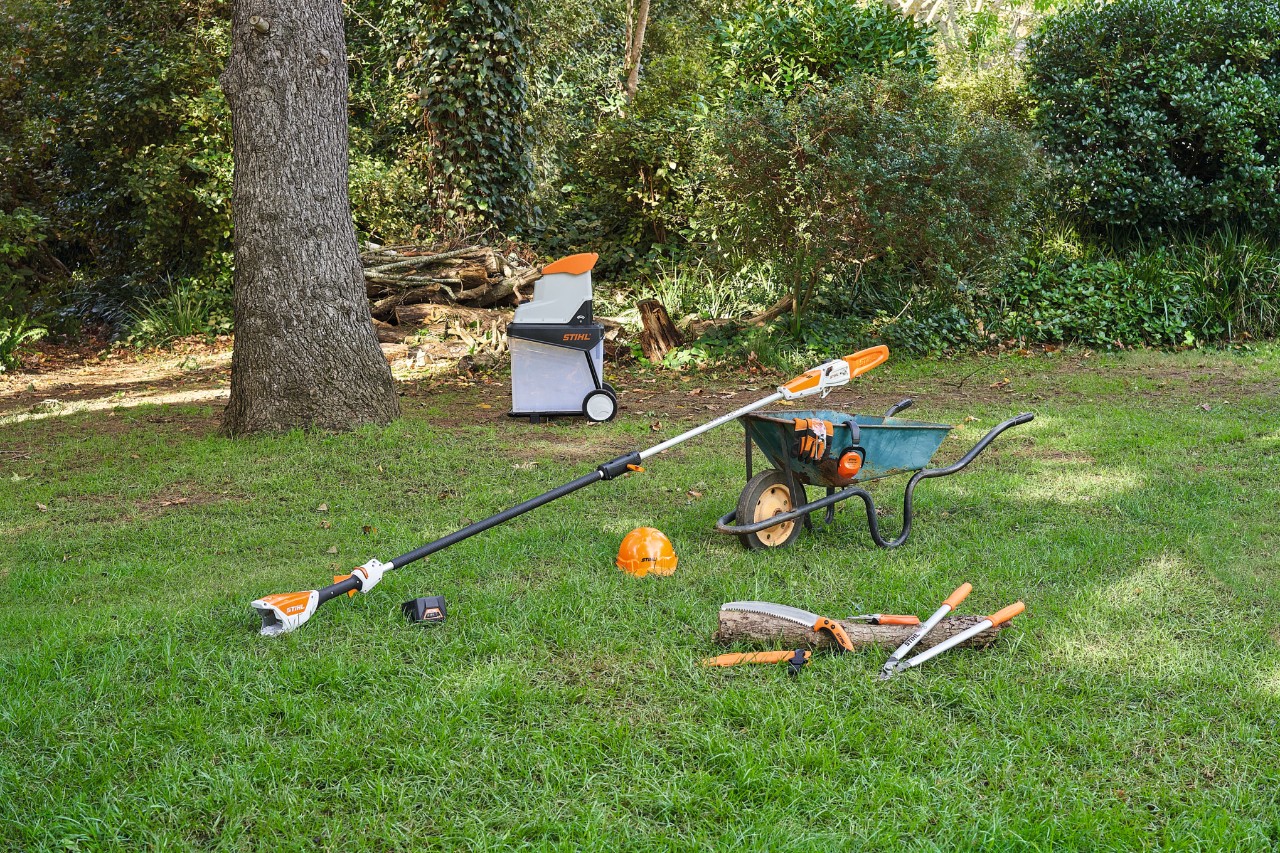 Vemos diversas herramientas, por ejemplo, unas tijeras de jardinero y de poda STIHL, sobre el césped de un jardín para podar un manzano.