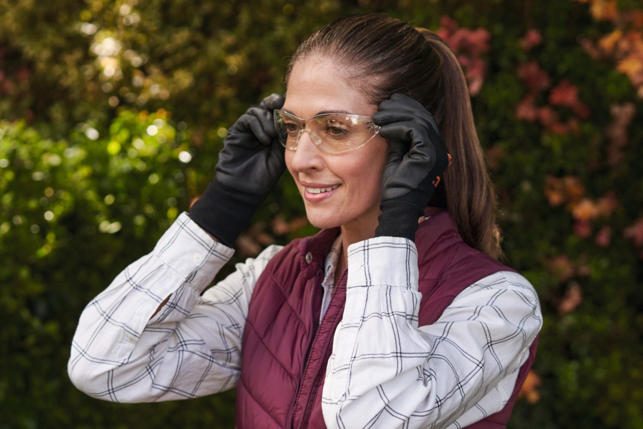 Una mujer de pelo marrón sonriente con guantes de protección se pone gafas de protección 
