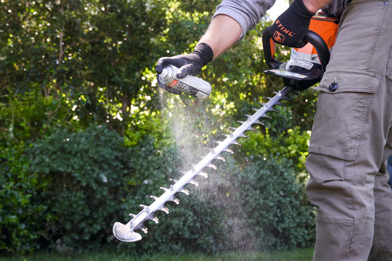 Un hombre rocía la tijera para setos de batería STIHL HSA 60 con Multiclean