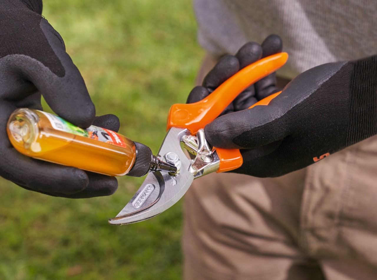 Una persona con guantes de trabajo STIHL lubrica unas tijeras de jardinero