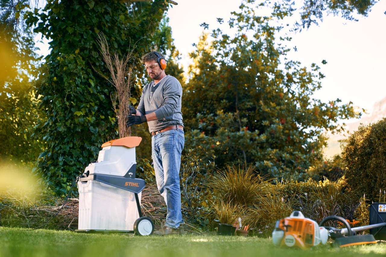 Un hombre con protección auditiva tritura ramas antes de compostar con una biotrituradora eléctrica STIHL GHE 140.