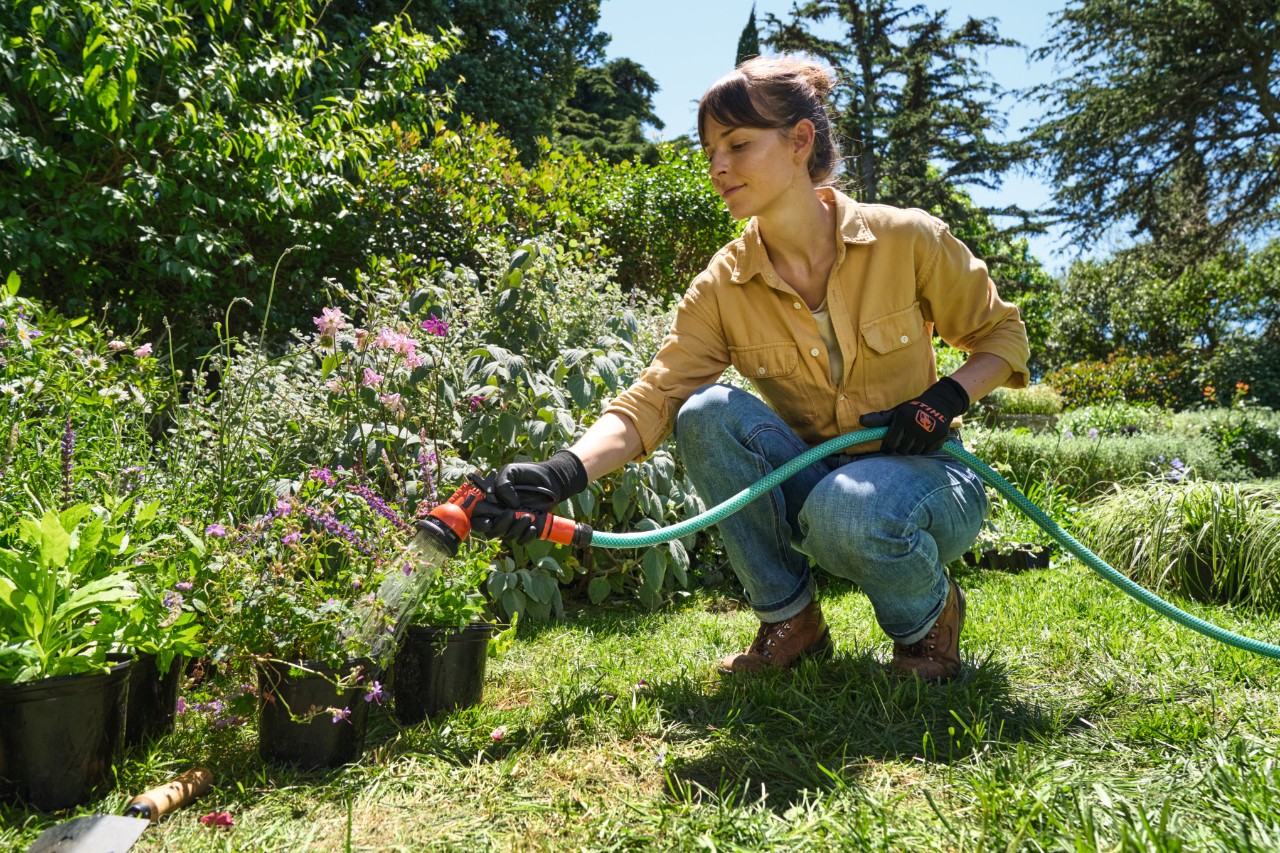 Una mujer en un césped riega plantas en maceta con una manguera de jardín