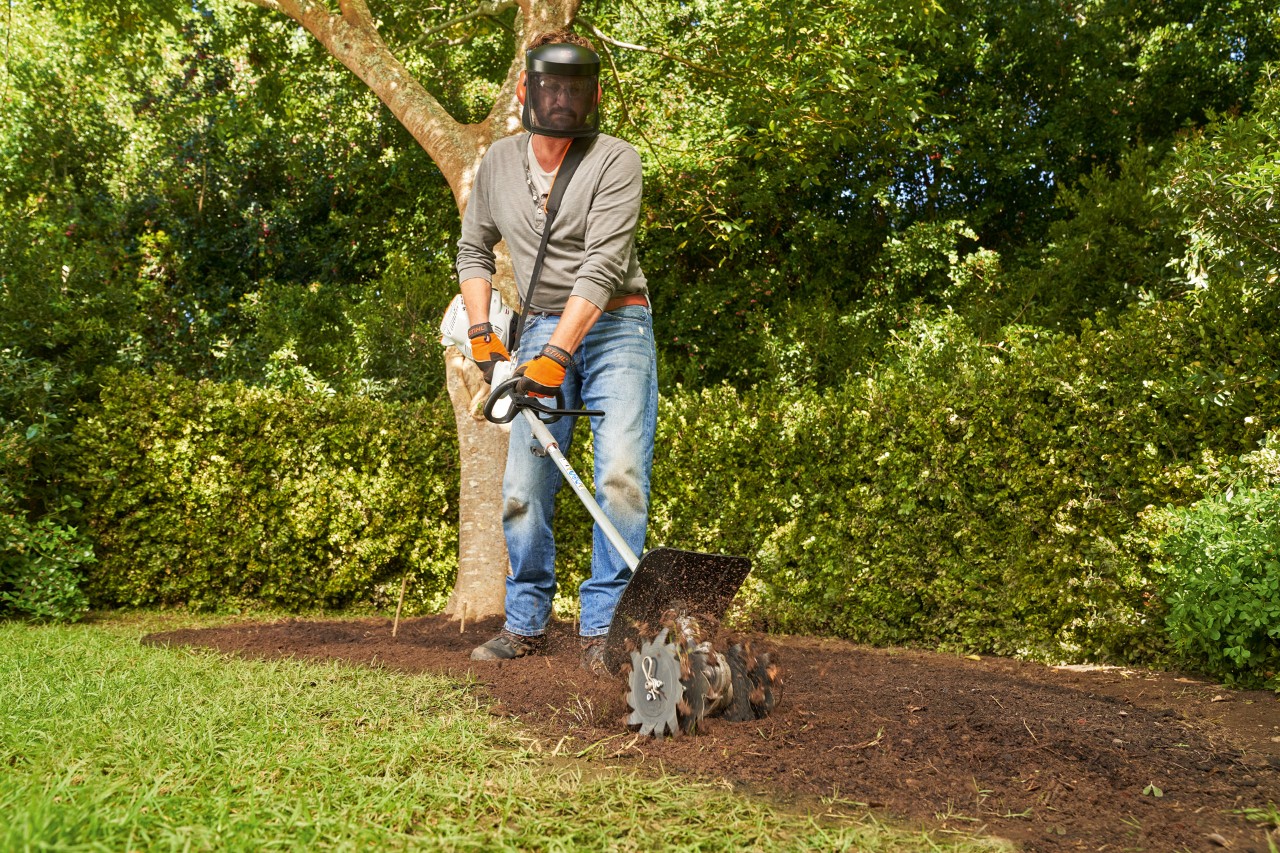 Un hombre trabaja el humus en el suelo con un sistema combinado STIHL KM 56 RC-E
