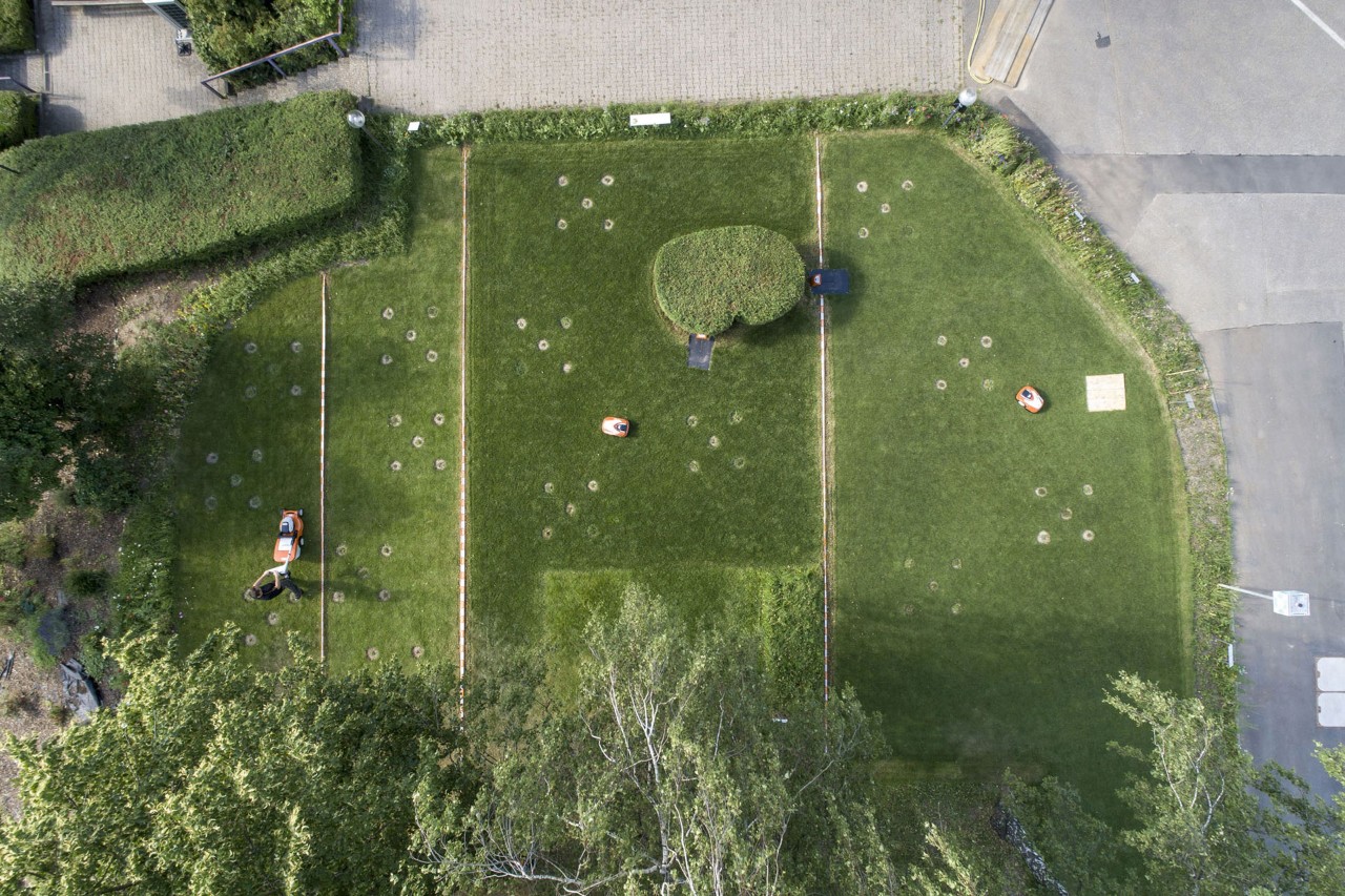 Vista desde arriba de un terreno dividido en cuatro partes con robots cortacésped STIHL y un cortacésped en las instalaciones de la fábrica