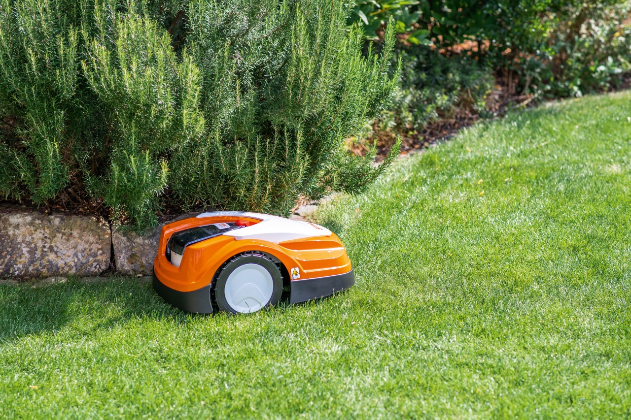 Un robot cortacésped STIHL iMOW® RMI 422 PC sobre césped verde junto a un borde para arriates de piedras planas