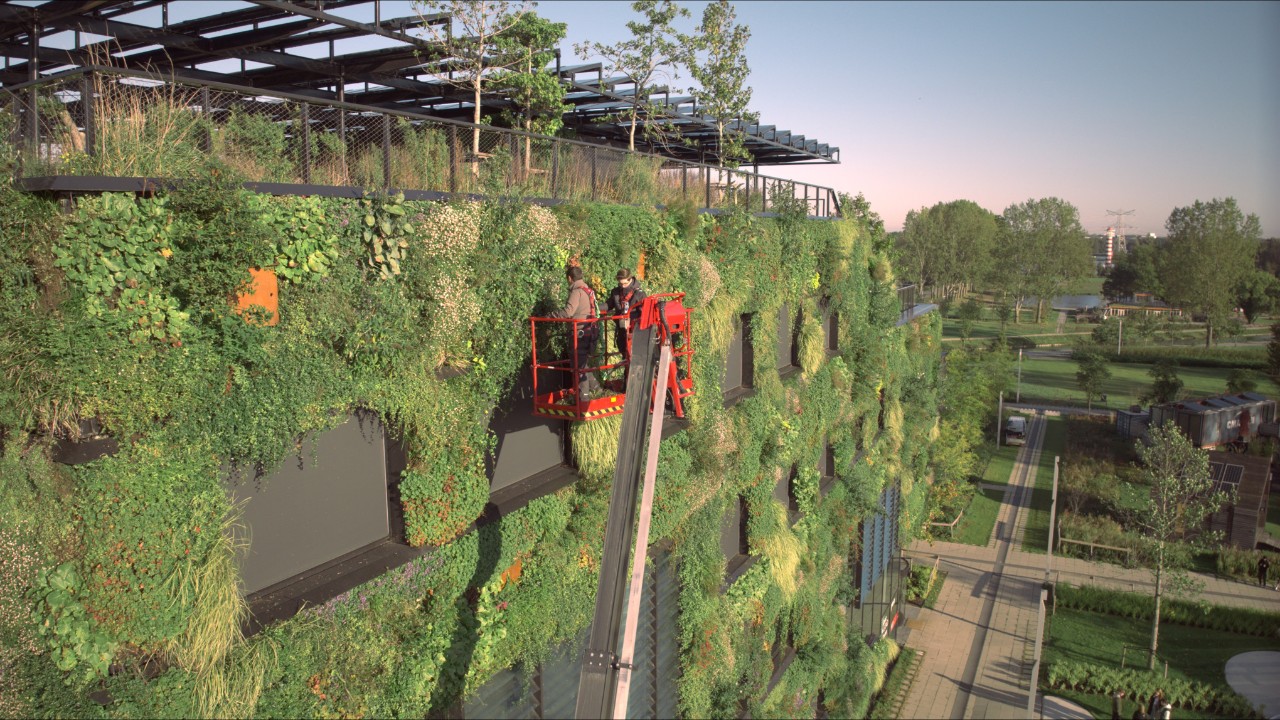 Dos jardineros trabajan subidos en una grúa en un jardín vertical de un edificio de oficinas