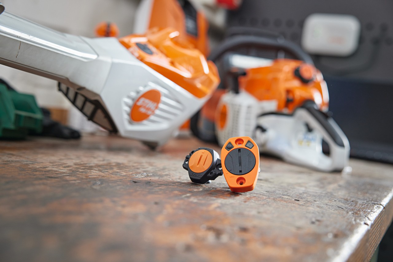 Sobre un banco de trabajo un STIHL Smart Connector y un STIHL Smart Connector 2 A. Se ven varias máquinas STIHL al fondo
