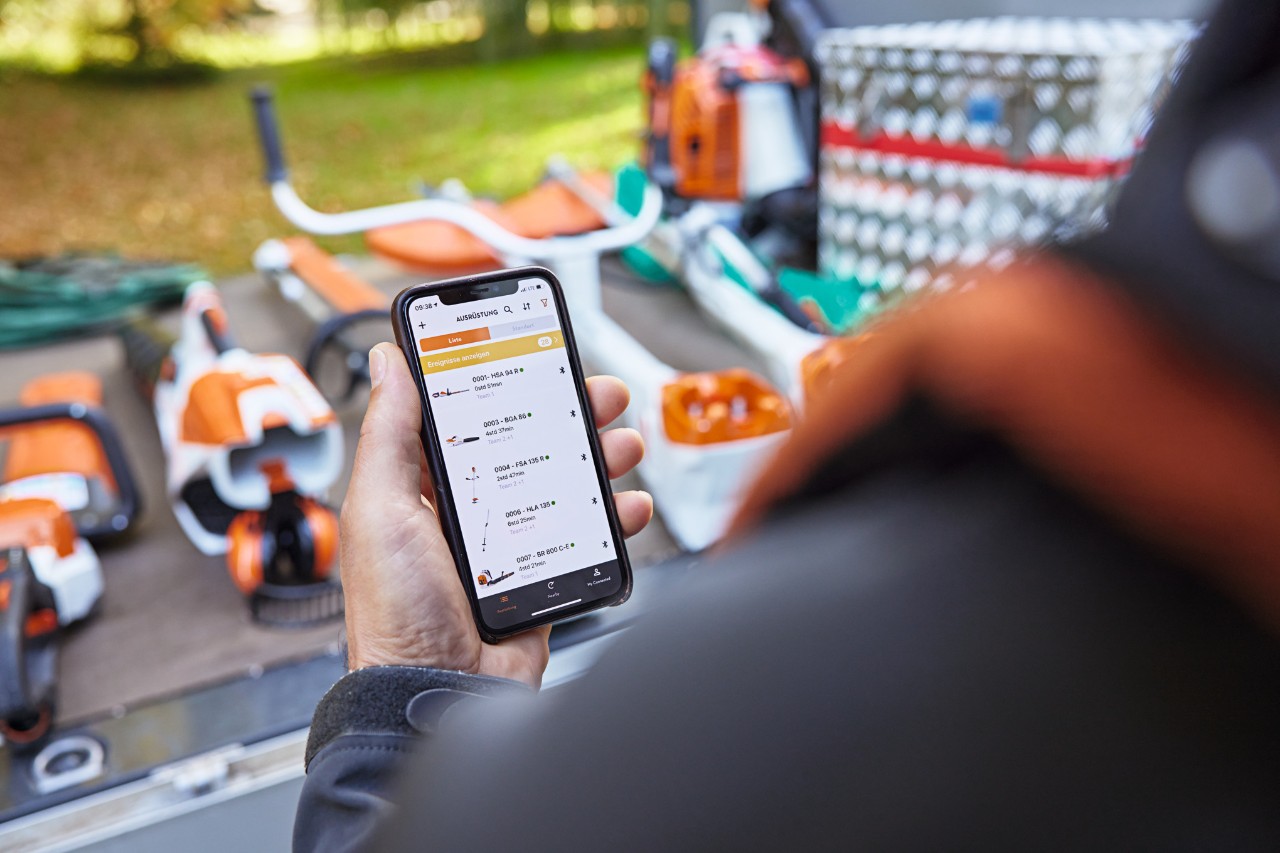 Una persona con un móvil con la STIHL Connected App y delante la plataforma de carga de un camión con varias máquinas 