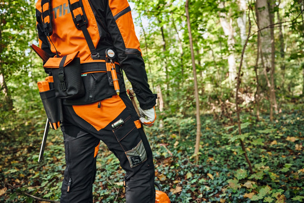 Un hombre trabajando en el bosque con una desbrozadora y llevando el sistema de arnés modular