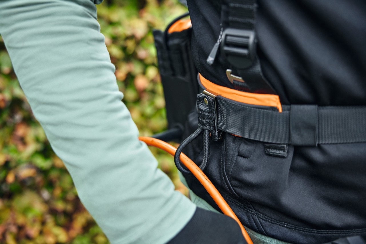 Una persona lleva el sistema de arnés modular STIHL ADVANCE X-Flex con una bolsa de batería con cable de conexión y guía de cables
