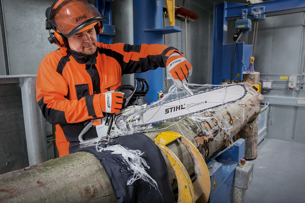 Un hombre haciendo una prueba de calidad anticorte de la ropa de protección STIHL con una motosierra STIHL