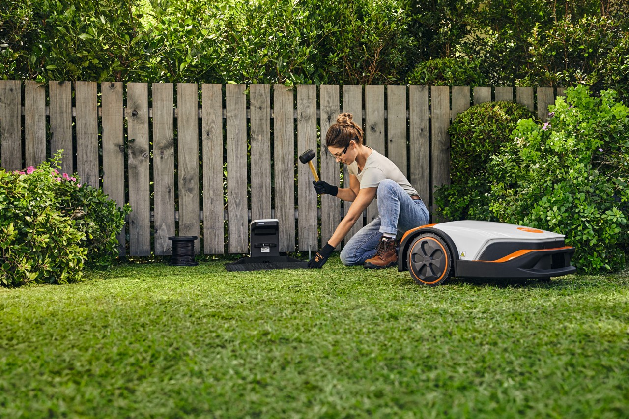 Una mujer instala la estación de conexión para su STIHL iMOW® delante de una valla en su propio jardín.
