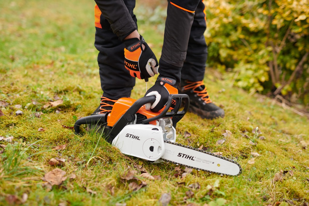 Una motosierra de arranque fácil STIHL MS 180 C-BE con ErgoStart; un usuario la pone en marcha sobre el césped.